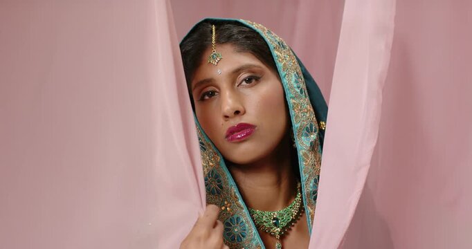 Woman using right-hand parting pink curtains adjusting teal scarf showing tikka necklace in studio