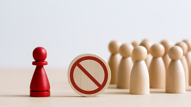 Red pawn standing separate from a group of wooden figures behind a prohibition sign depicting social exclusion, discrimination, and rule