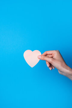 Hand hold pink paper heart against blue background