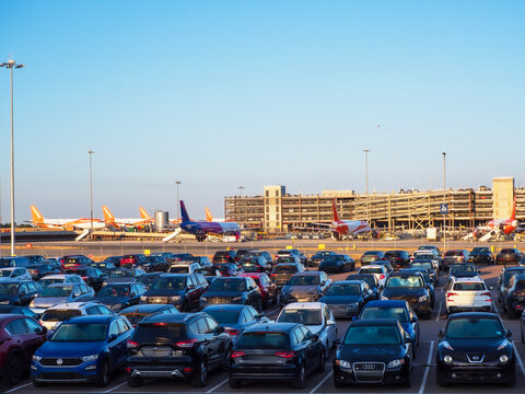 Luton, UK - August 22nd 2026: Airport apron with parked passenger jets, boarding stairs, and cars in multilevel parking garage