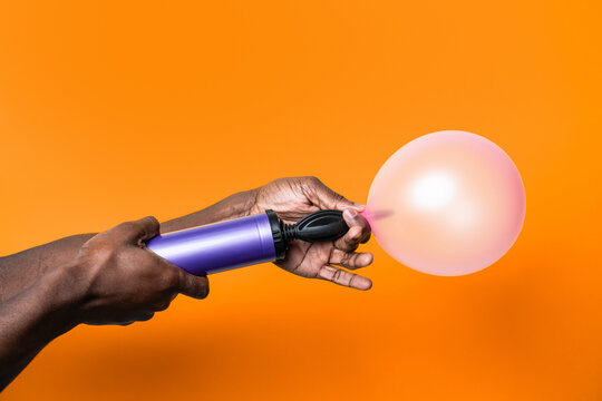 Hand inflate pink balloon with purple pump on orange background