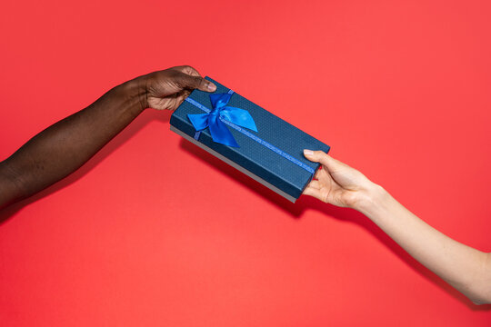 Multiethnic hands exchange blue gift box on red background