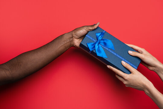 Multiethnic hands exchange blue gift box on red background