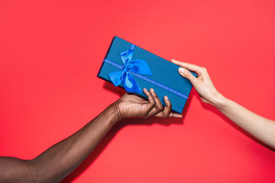 Diverse hands exchange blue gift box on red background