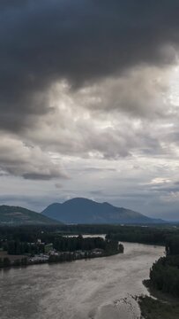 Aerial View of Fraser River Winding Through Chilliwack, British Columbia with Majestic Mountains and Dramatic Clouds