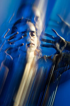 Woman with closed eyes behind abstract blue glass