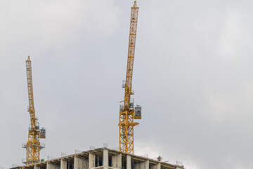 Construction cranes rise against a cloudy sky at a city site during a busy morning © beholdereye