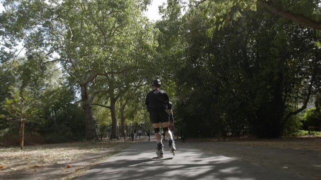 A skater speeds up in Battersea Park, London on a sunny autumn day with his rollerblades