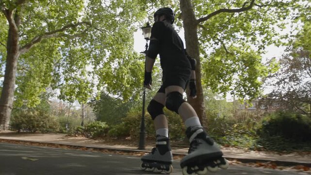 A skater speeds up in Battersea Park, London on a sunny autumn day with his rollerblades