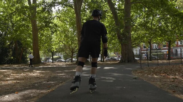 A skater speeds up in Battersea Park, London on a sunny autumn day with his rollerblades