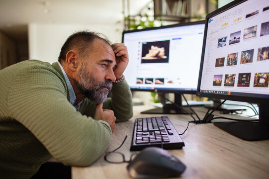 Middle-aged man reviewing photos on dual monitors at home office