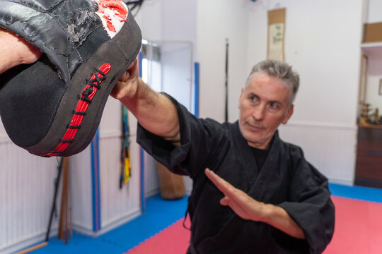 Hapkido student in a black uniform training martial arts with a focus mitt during a self-defense session in the dojang