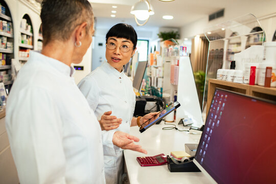 Two pharmacists discussing prescriptions at pharmacy counter with tablet