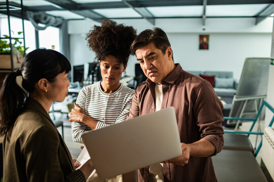 Diverse coworkers discussing project on laptop in modern office