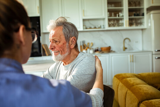 Female caregiver comforting elderly man at home kitchen