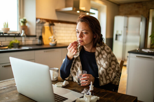Woman taking medicine while working from home kitchen