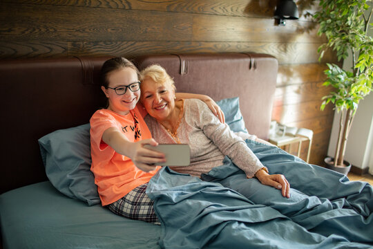 Granddaughter taking selfie with grandmother in bed at home