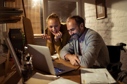 Man in wheelchair and woman collaborating on laptop in home office