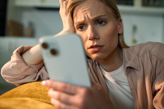 Worried woman reading bad news on smartphone at home