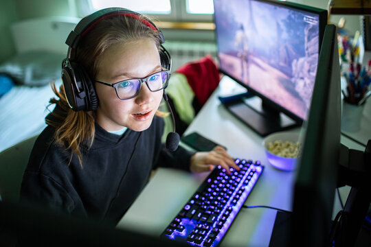 Teen girl gamer with headset playing pc at home desk