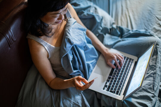 Woman shopping online with credit card in bed at home
