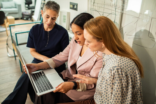 Three businesswomen collaborating on laptop in modern office