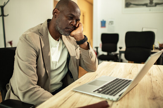 Middle-aged man looking tired at laptop in office
