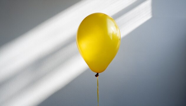 a single bright yellow balloon floats against a white background with dappled light