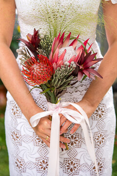 Bride fashion details. Crochet wedding dress and exotic wedding bouquet made of Protea, Leucospermum (Pincushion Protea), Brunia in the hands of the model.