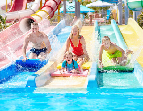 A happy family racing down colorful water slides on mats at a water park.