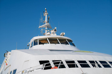 White passenger ferry viewed from the front with bridge windows, navigation equipment and antennas against a clear blue sky © Anna Zaro