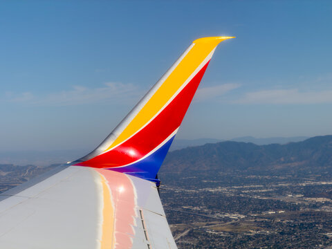 BURBANK, CA, APR 28, 2026: Aerial view from window of Southwest winglet in flight, red-yellow-blue livery, sunlit tip, with hazy mountains and Los Angeles city sprawl below