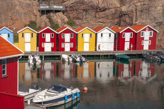 Row of vibrant red, yellow, and white wooden fishing huts along Sm&Atilde;&para;gen pier with small motorboats docked in the harbor during daylight.