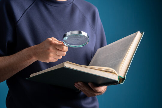 A person is holding an open scripture and a magnifying glass.