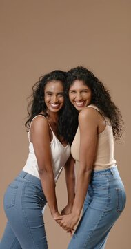 Vertical video: African American  and  Indian women smiling in tanks laughing holding hands on set