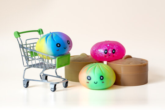 Three colorful dumpling shaped squishy toys with miniature shopping cart and plastic steamer baskets on beige background