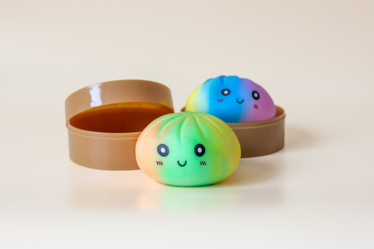 Two colorful dumpling shaped squishy toys with smiling faces and plastic steamer baskets on beige background