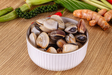 Fresh raw clams in white bowl on wooden table surrounded by green peppercorns, turmeric, and other healthy cooking ingredients © Andrei Starostin