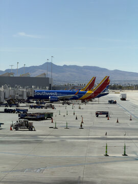 LAS VEGAS, NV, APR 28, 2026: Two Southwest jets nose-to-tail at gates with desert mountains behind, ground crew and equipment scattered across the sunlit tarmac, Harry Reid International Airport