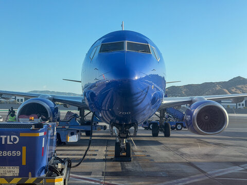 BURBANK, CA, APR 28, 2026: Head-on view of a Southwest Boeing 737 nose parked at Burbank Airport gate, ground service equipment and TLD cart in foreground, mountains in background under clear sky