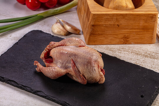Raw whole quail on black slate with fresh garlic, green onions, and tomatoes, gourmet poultry preparation