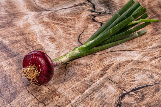 Fresh red onion with green stalks on rustic wood