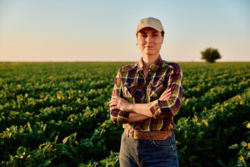 Obraz na płótnie Canvas Woman farmer standing with arms crossed in a green agricultural soybean field, representing agriculture and rural industry