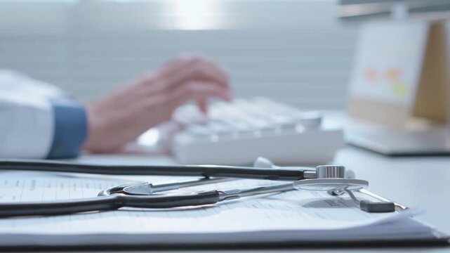 Medical professional working on computer beside stethoscope during healthcare consultation.