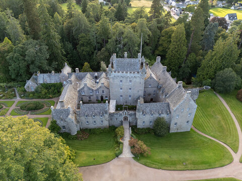 Elevated frontal aerial drone photo of Cawdor Castle facade, stone entrance bridge, lawn, and formal gardens near Nairn in Highland, Scotland