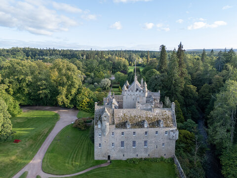Elevated wide aerial drone photo of Cawdor Castle, stone facade, turrets, and lush forest grounds near Nairn in Highland, Scotland
