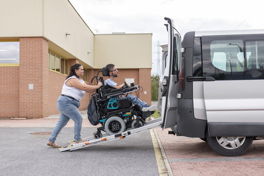 Personal assistant accompanying a powered wheelchair user into an adapted vehicle using an accessible ramp.