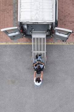 Personal assistant helping a man with disability leave an adapted vehicle using an accessible wheelchair ramp.