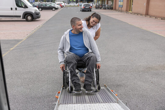 Powered wheelchair user boarding an adapted vehicle with support from an assistant and an accessible ramp.