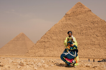 Tanoura costume male performer holds colorful spinning skirt mid swirl standing before the Great Pyramids of Giza on the sandy Egyptian desert plateau © .shock